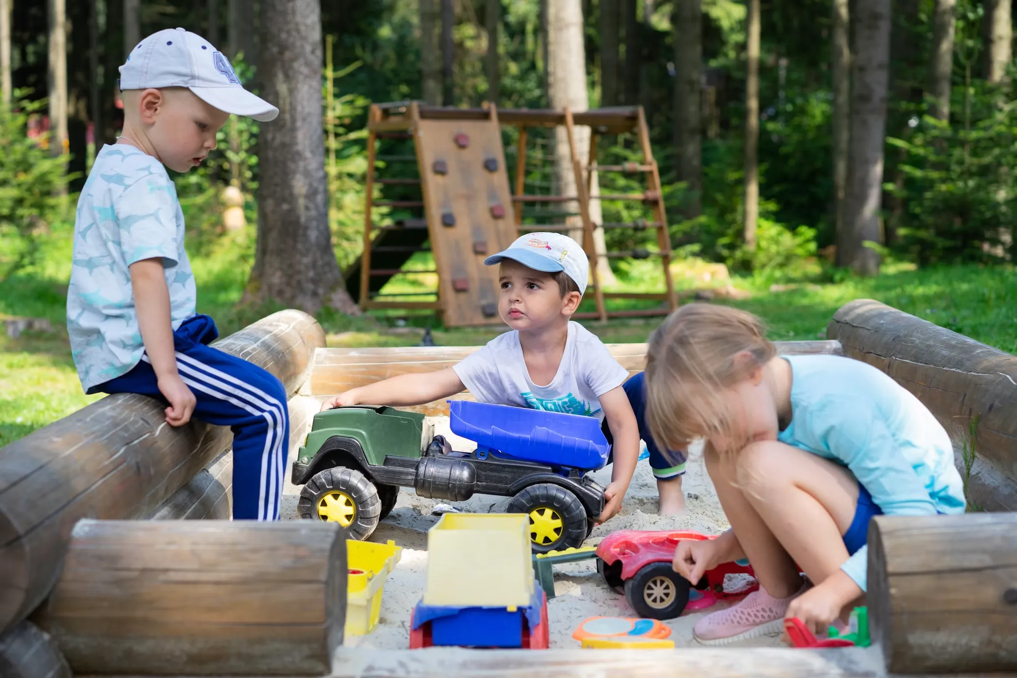 Kids sharing toy trucks in a sandbox